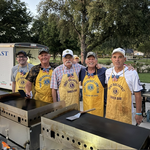 Tracy Breakfast Lions Club volunteers standing at outdoor griddles during a Fourth of July pancake breakfast.